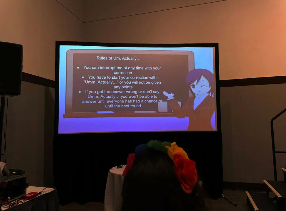 Um, Actually Rules proyectadas en la pantalla con un personaje de anime presentándolas.  Reglas de Um, en realidad... Puedes interrumpirme en cualquier momento con tu corrección. Tienes que comenzar tu corrección con 'Um, en realidad...' o no recibirás puntos. Si obtienes la respuesta incorrecta o no digas 'Um, en realidad'... no podrás responder hasta que todos hayan tenido la oportunidad de responder o hasta la siguiente ronda.