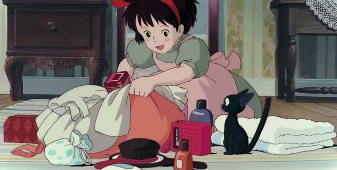 Kiki empacando sus cosas con Jiji sentado a su lado.