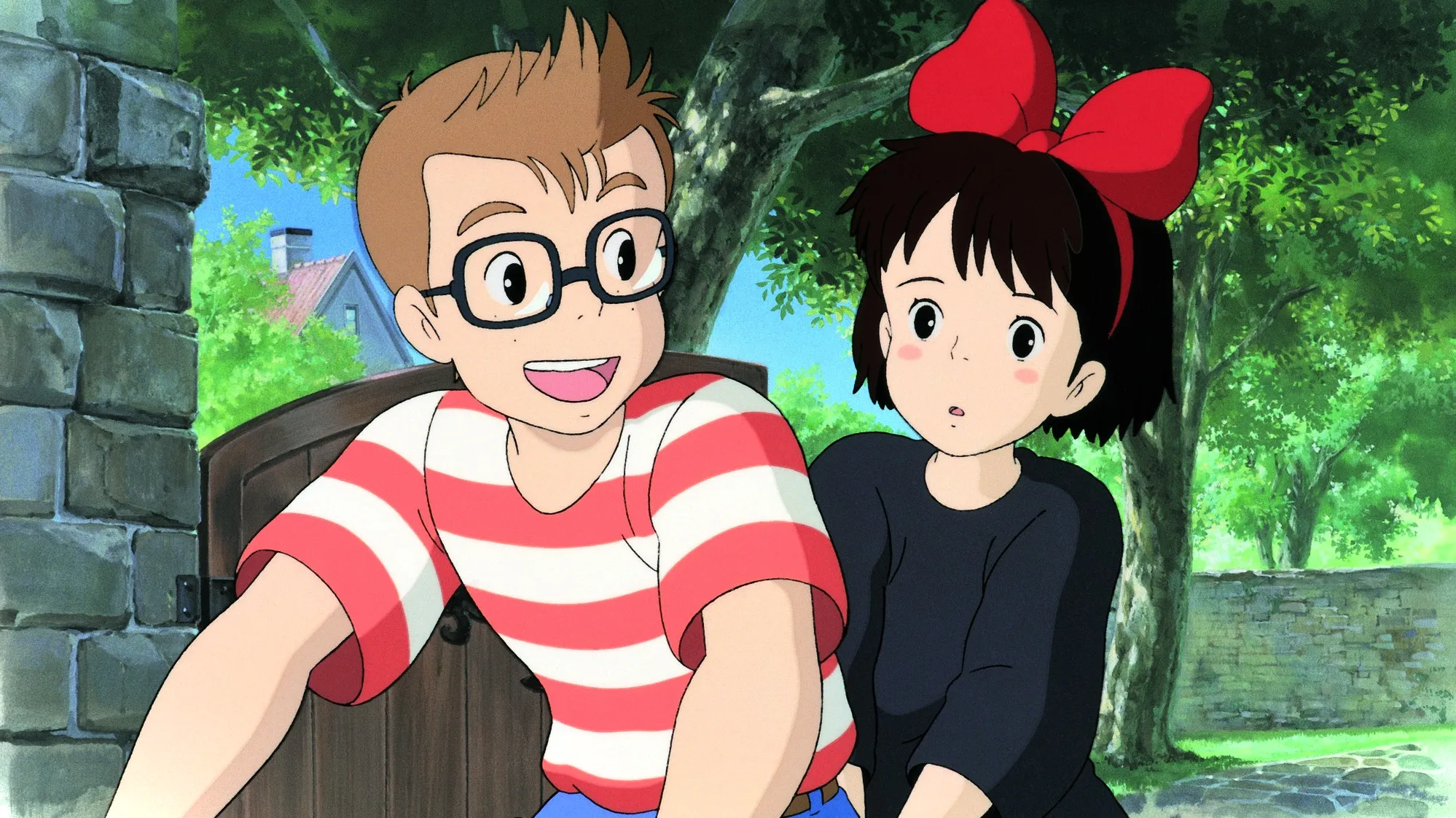 Kiki montando una bicicleta detrás de Tombo, quien le devuelve la sonrisa.