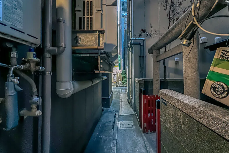 El mismo callejón estrecho, pero ahora frente a la entrada del santuario a la derecha.  La entrada tiene dos puertas rojas abatibles.